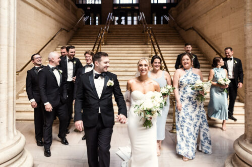 Candid photo of summer wedding party walking through Union Station wearing tuxedos and light blue floral print