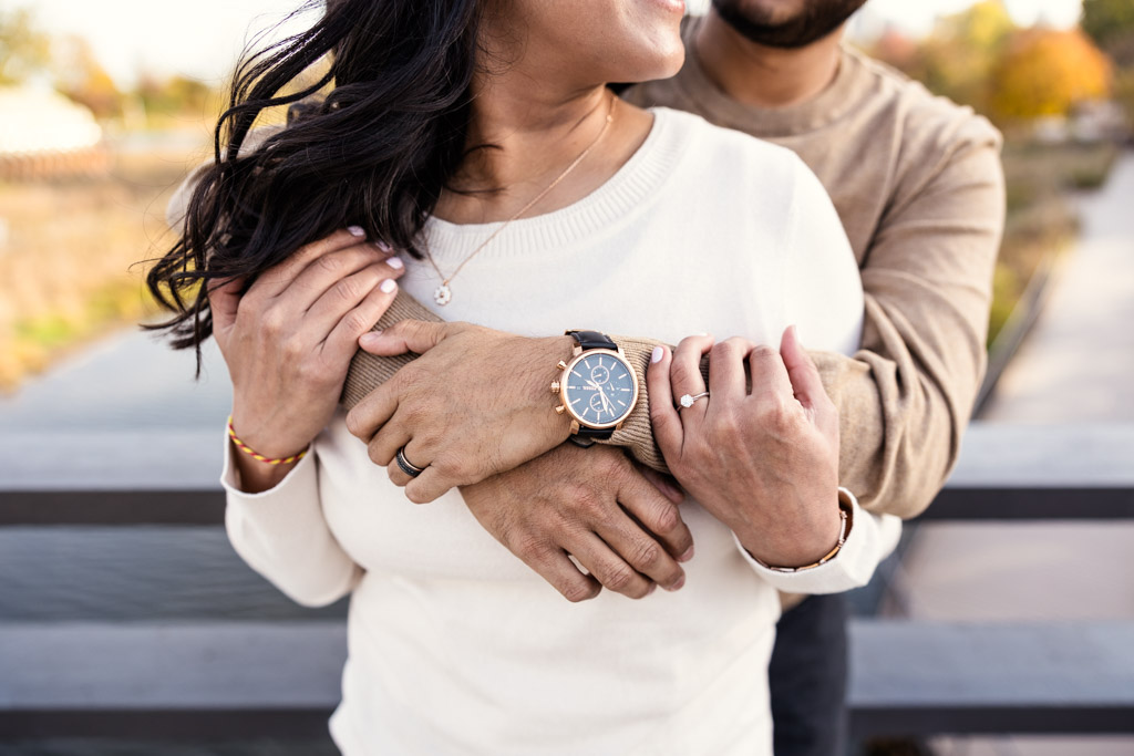 Photo of engaged couple embracing on a Lincoln Park bridge, focused on their hands and rings