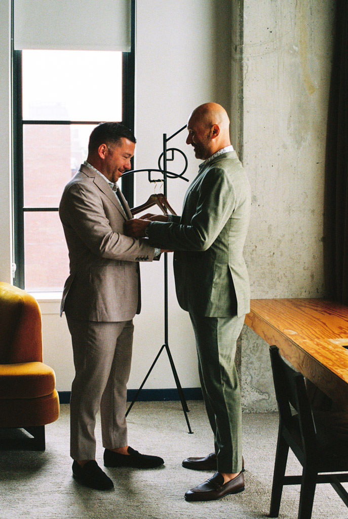 Two people in suits exchange a book in a room adorned with modern decor and a large window, capturing the moment like a scene from classic film photography.