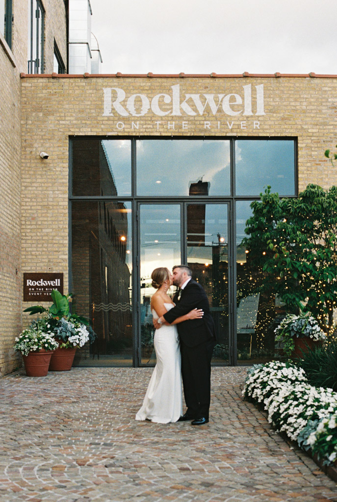 Just married bride and groom kiss outside the entrance to Rockwell on the River wedding venue captured on 35mm film