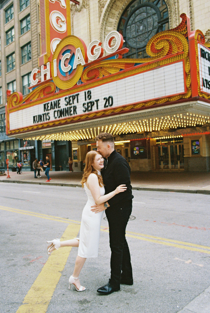 A couple embraces on a street in front of the iconic Chicago Theatre marquee, captured beautifully in film photography.