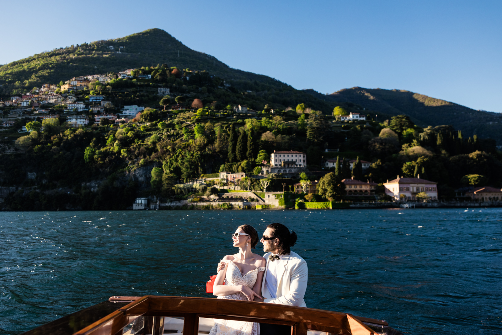 Bride and groom watch sunset from boat on Lake Como with historic Italian wedding venue Villa Pizzo in the background