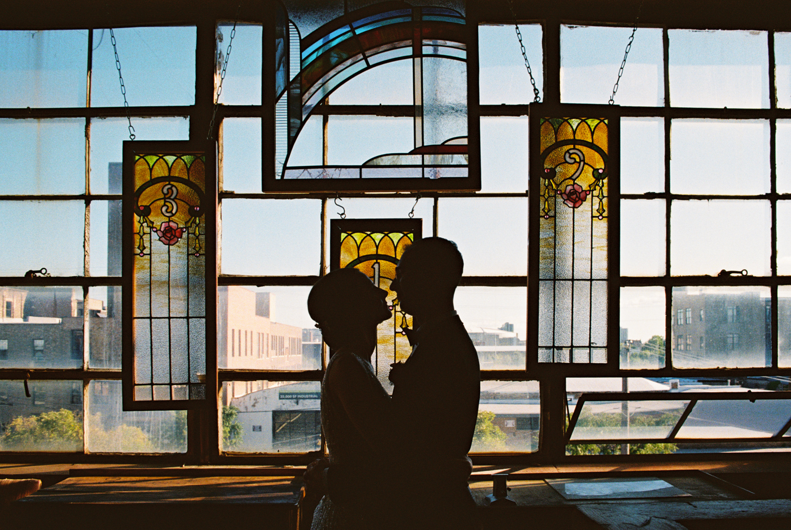 Romantic silhouette photo of bride and groom standing in front of vintage stained glass windows at Salvage One wedding venue on 35mm film