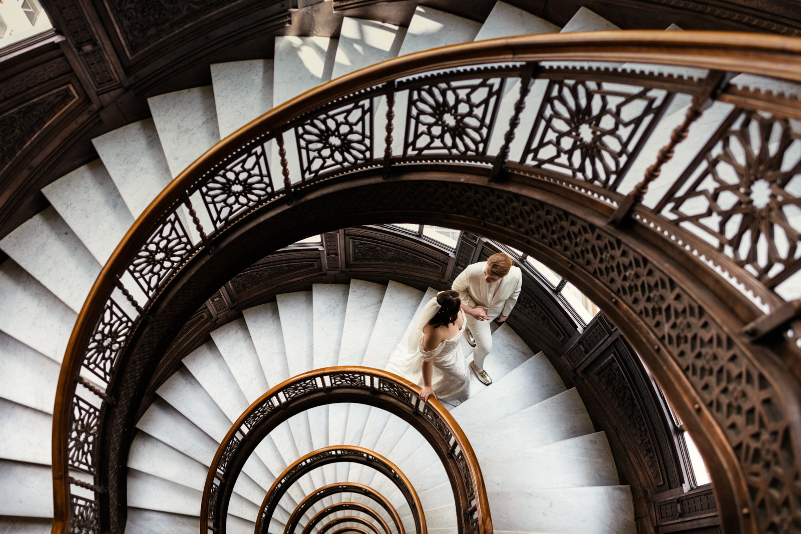 Creative wedding photo of two brides walking up spiral staircase at The Rookery Building downtown Chicago