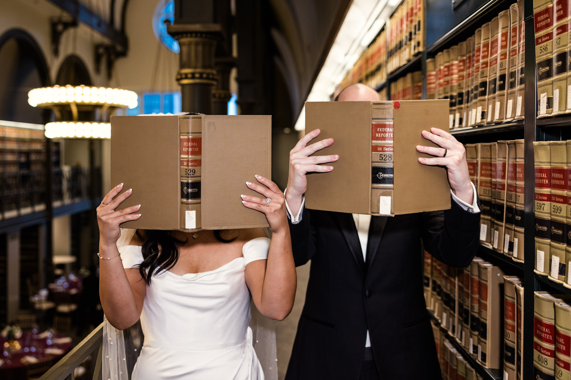 Creative wedding photo of bride and groom holding books in front of their faces while showing off wedding bands at their Chicago library wedding