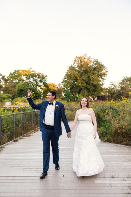 Bride and groom in wedding attire walk hand in hand along a path in Lincoln Park
