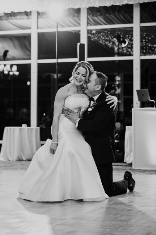 Bride and groom dancing joyfully, the groom kneels and embraces the bride on a well-lit ballroom floor at their Lincolnshire Marriott Resort wedding reception
