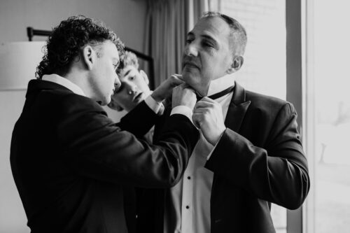 Two groomsmen in suits adjust their dad's bow tie in front of a window at Lincolnshire Marriott Resort wedding