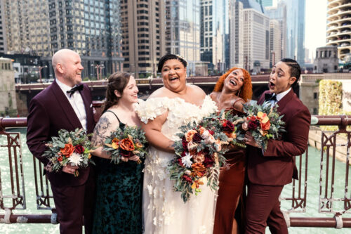 Bride and wedding party dressed in fall colors with jewel toned bouquets laugh on Chicago bridge before Osteria Via Stato wedding