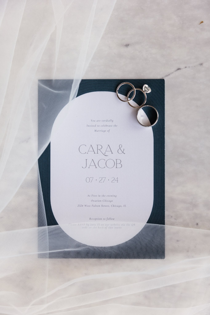 Wedding invitation, three rings and veil on a marble surface