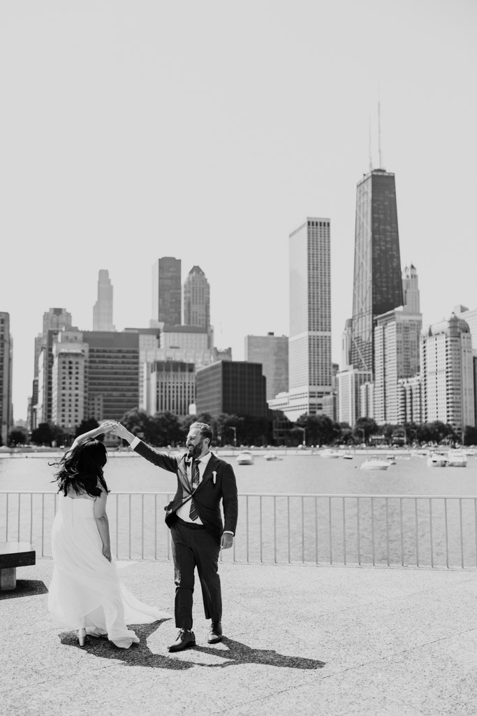 Black and white photo of bride and groom dance on the lakefront with the Chicago skyline in the background