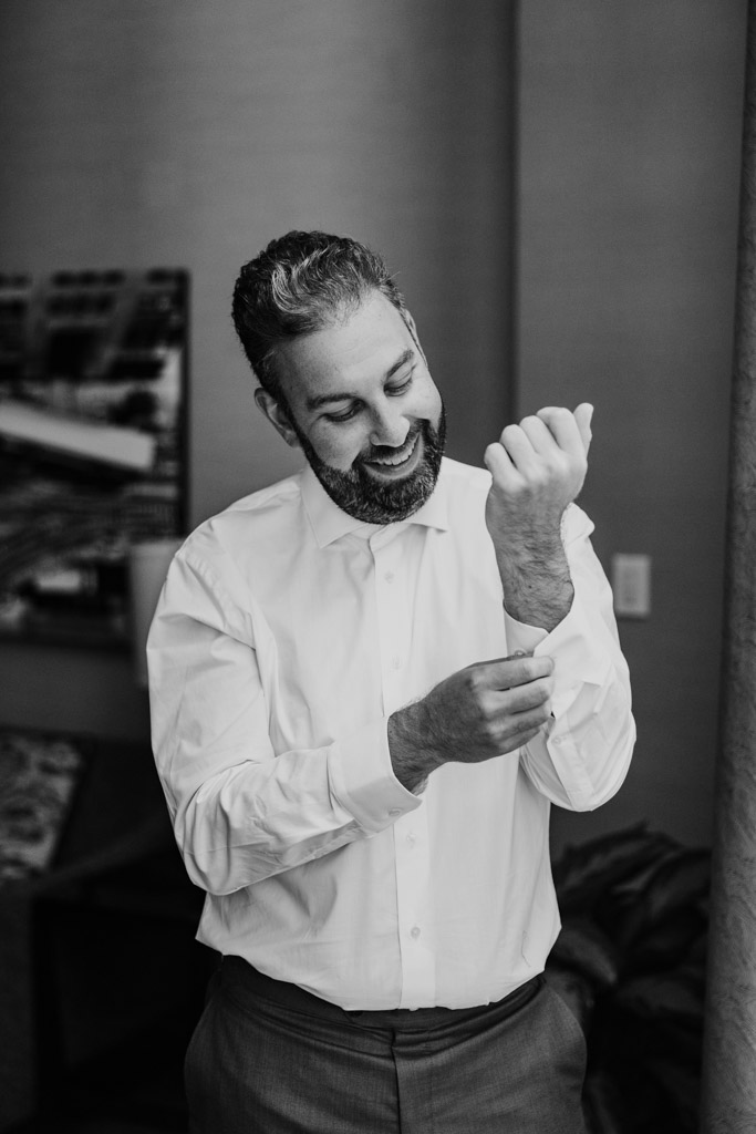 Black and white photo of groom adjusting his shirt cuff while getting ready at the Westin River North in downtown Chicago