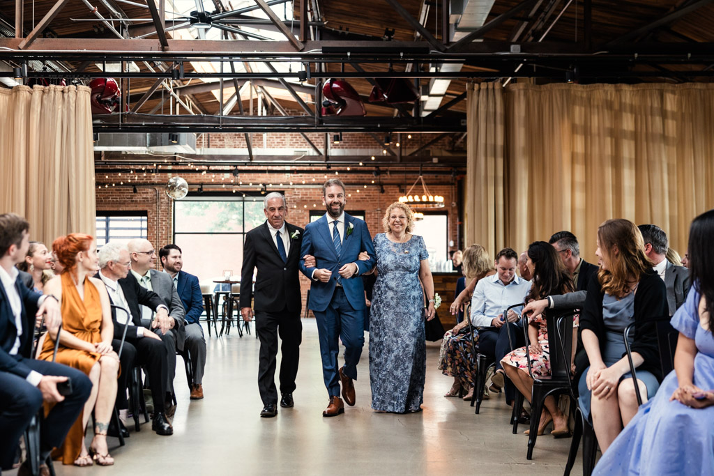 Groom walks down the aisle with his parents as guests look on during Ovation Chicago wedding ceremony