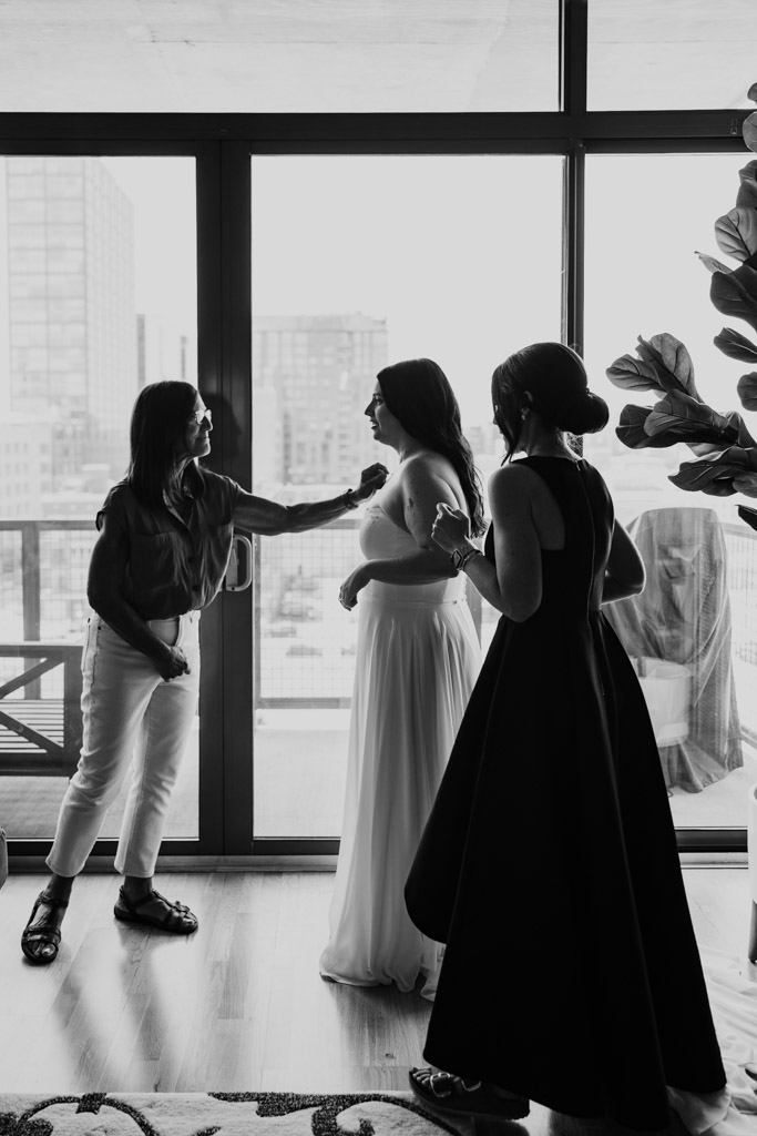 Black and white photo of two women heling the bride with her dress while getting ready at the Westin River North in downtown Chicago
