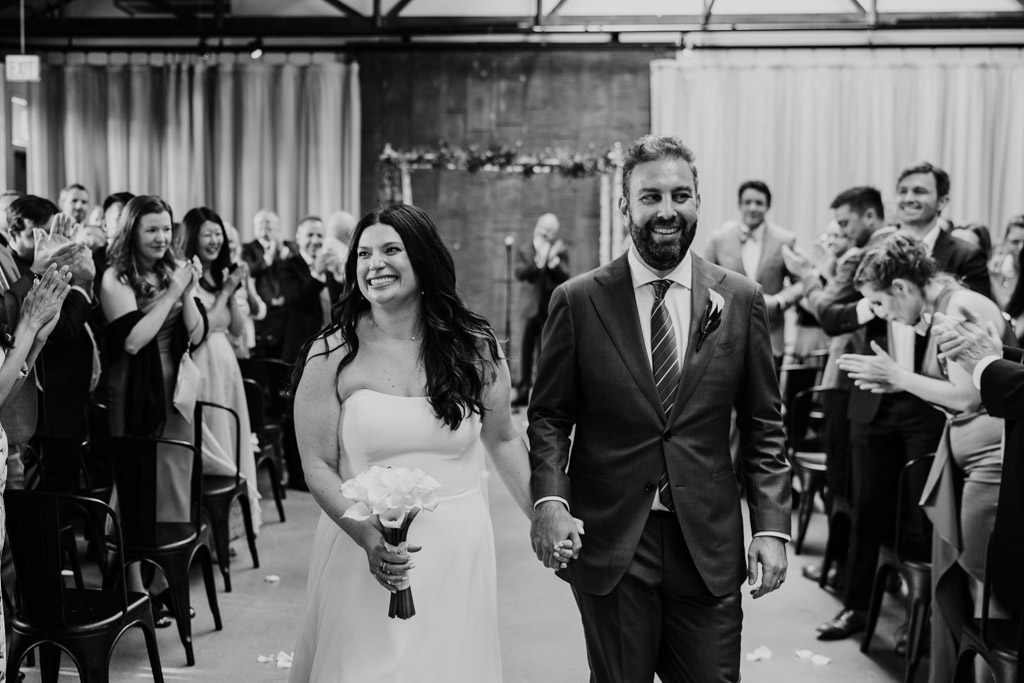 Black and white photo of bride and groom walking down the aisle after their Ovation Chicago wedding ceremony