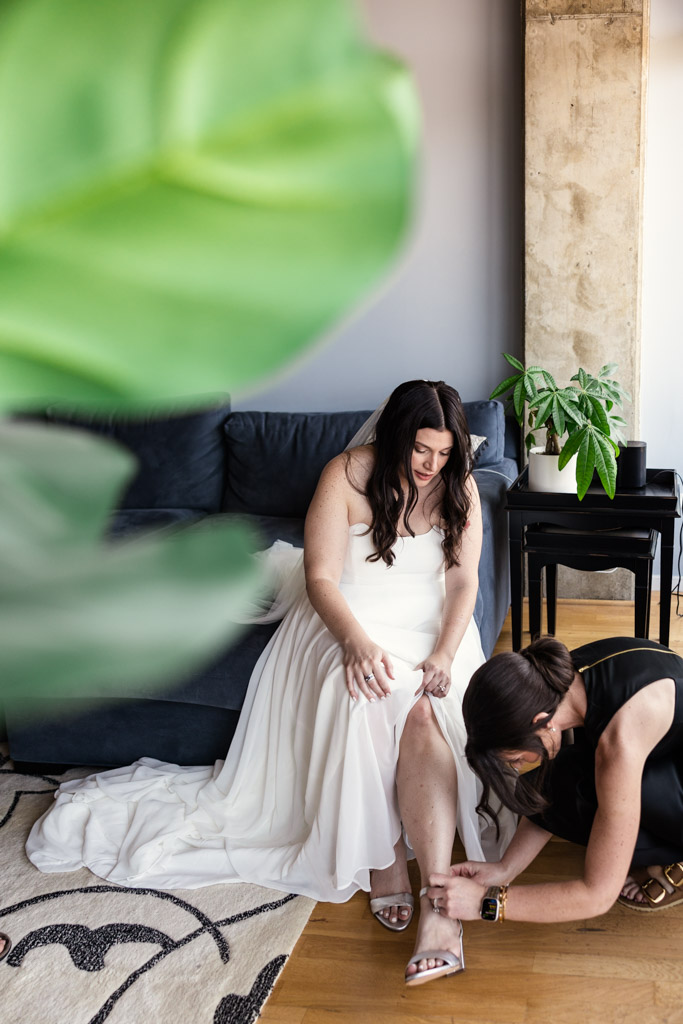 Bride sits on a couch as the Maid of Honor helps adjust her shoes as they get ready at the Westin River North in downtown Chicago