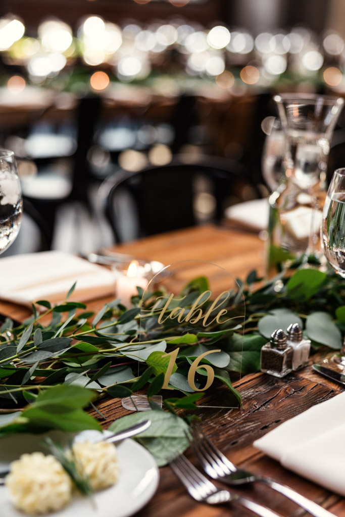 Guest table setting with greenery centerpiece, exquisite glassware, and table number 16 for wedding reception at Ovation Chicago