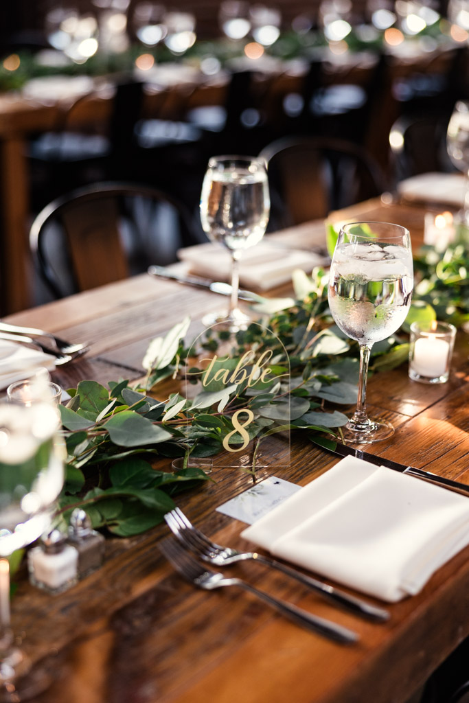 Wooden guest table setting with greenery, glassware, candles, and a 