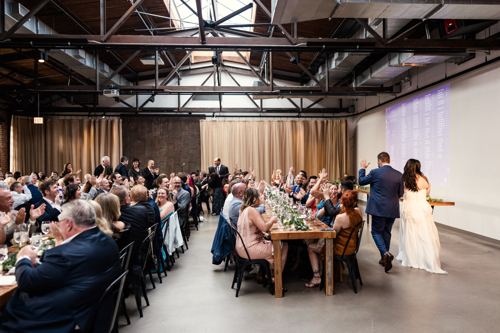Bride and groom enter their Ovation Chicago wedding reception with guests seated at long tables