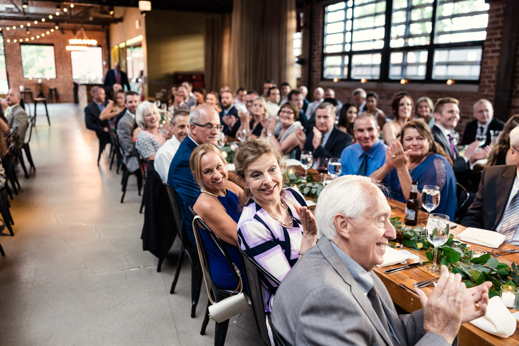 Guests sitting at long dining tables listening to speeches during wedding reception at Ovation Chicago