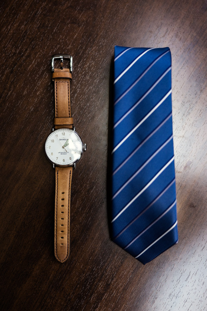 Groom's watch with brown leather strap and blue striped tie arranged on a wooden table