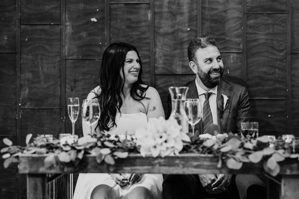 Black and white photo of newlywed couple listening to speeches while seated at the head table during their Ovation Chicago wedding reception