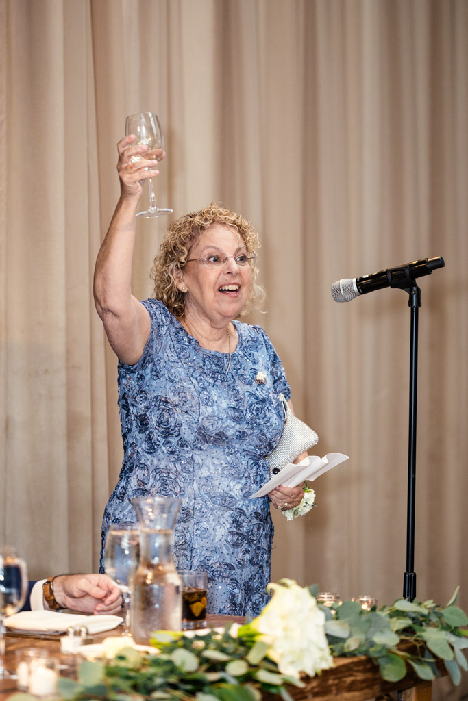 Mother of the bride in a blue dress raises her glass with a toast during Ovation Chicago wedding reception