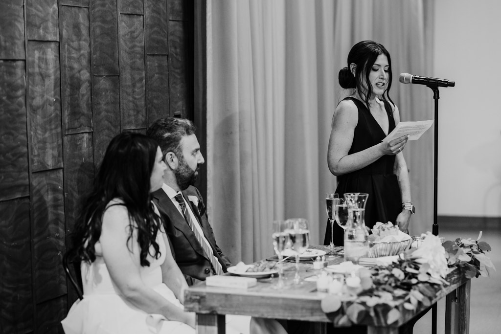 Black and white photo of newlyweds listening to Maid of Honor give speech Ovation Chicago wedding reception