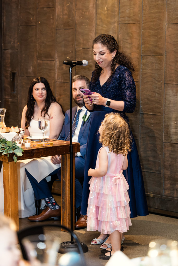 Woman gives speech at Ovation Chicago wedding reception while bride, groom and a young girl in a pink dress listen