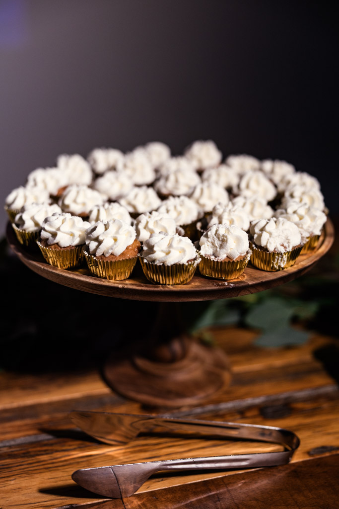 A wooden stand with cupcakes topped with white frosting, set on a wooden table for Ovation Chicago wedding reception