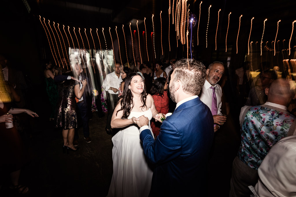 Bride and groom dance during Ovation Chicago wedding reception, with guests around them and string lights overhead