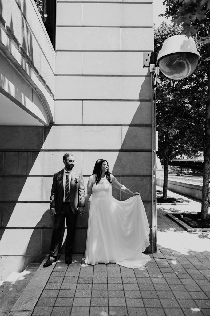 Black and white portrait of bride and groom standing hand in hand against a sunlit wall on the Chicago Riverwalk before their Ovation Chicago wedding
