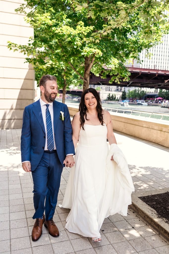 Bride and groom in wedding attire walks hand in hand along the Chicago Riverwalk