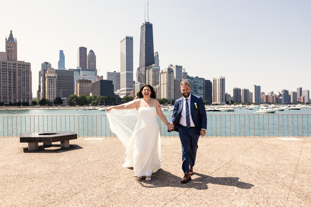 Bride and groom walk along the lakefront, with Chicago skyline behind them before their Ovation Chicago wedding