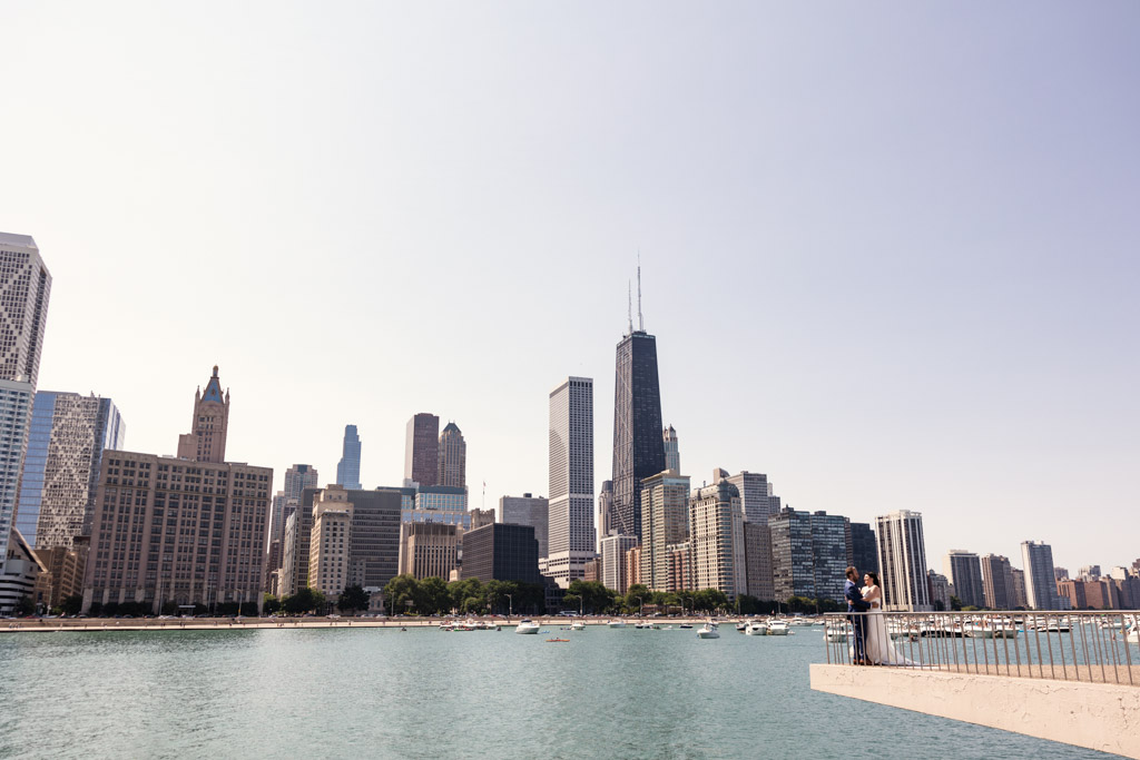 Bride and groom stand on a lakeside platform with Chicago skyline in the background before their Ovation Chicago wedding