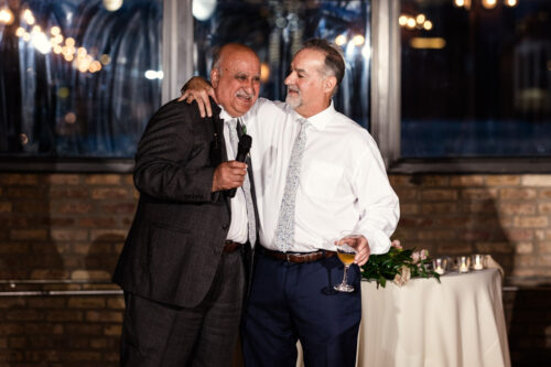 Newlyweds' fathers smiling and embracing during wedding reception at The Hive on Hubbard in Chicago