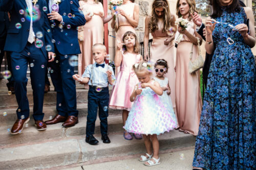 Children and adults blowing bubbles at a formal outdoor event, with a stone building in the background.