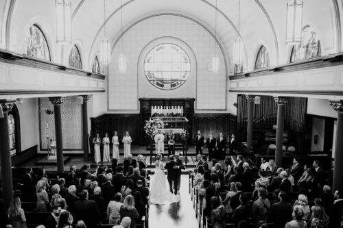 Black and white photo of groom embracing bride's father during wedding ceremony at Wicker Park Lutheran Church in Chicago