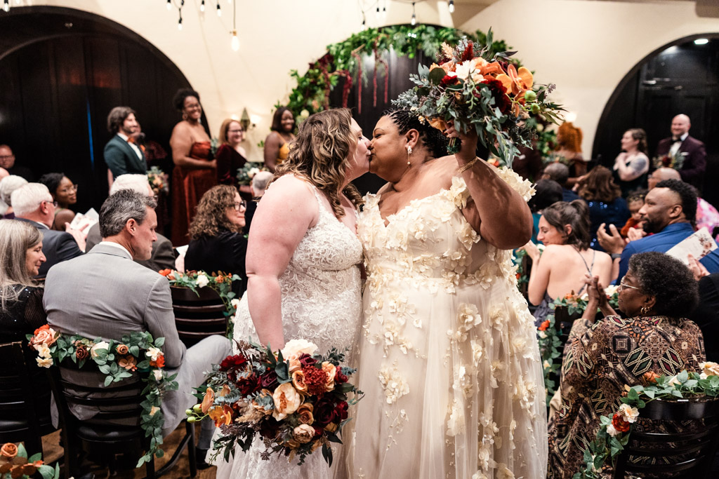 Brides kiss in the aisle after their wedding ceremony at Osteria Via Stato in downtown Chicago