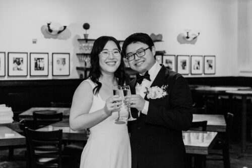Black and white portrait of newlyweds toasting with champagne glasses at Osteria Via Stato in downtown Chicago