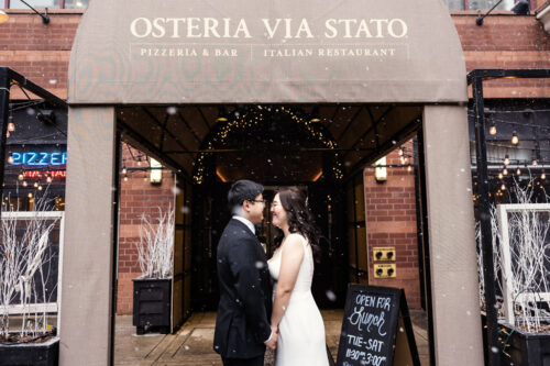 Bride and groom look into each others' eyes under the gently falling snow outside Osteria Via Stato before their Chicago winter wedding celebration