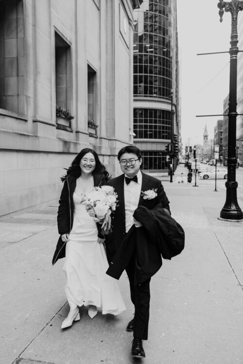 Black and white photo of bride and groom smiling and walking through downtown Chicago