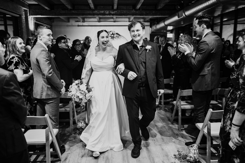 Just married bride and groom exit their New Year's Eve wedding ceremony at Walden Chicago while smiling and guests cheering