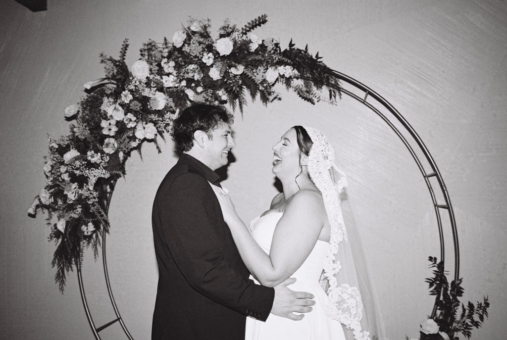 Bride and groom joyfully laugh under a floral arch at Walden Chicago during their wedding ceremony.