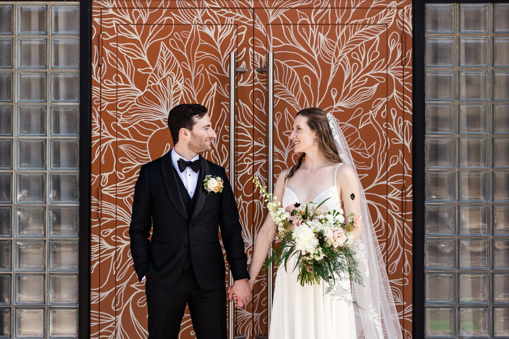 Bride and groom holding hands in front of a floral-patterned mural at The Arbory Chicago wedding venue