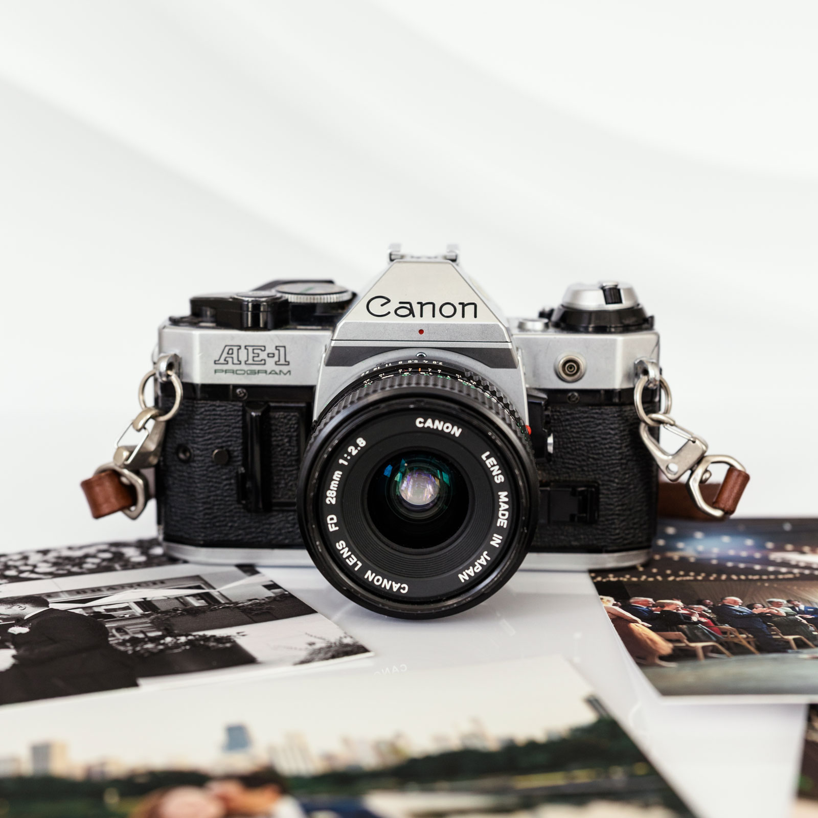 A classic camera sits in close-up, its reflection shimmering on a silver surface, embodying the skill of a documentary wedding photographer. Surrounded by sentimental photographs, it captures timeless moments artfully preserved.