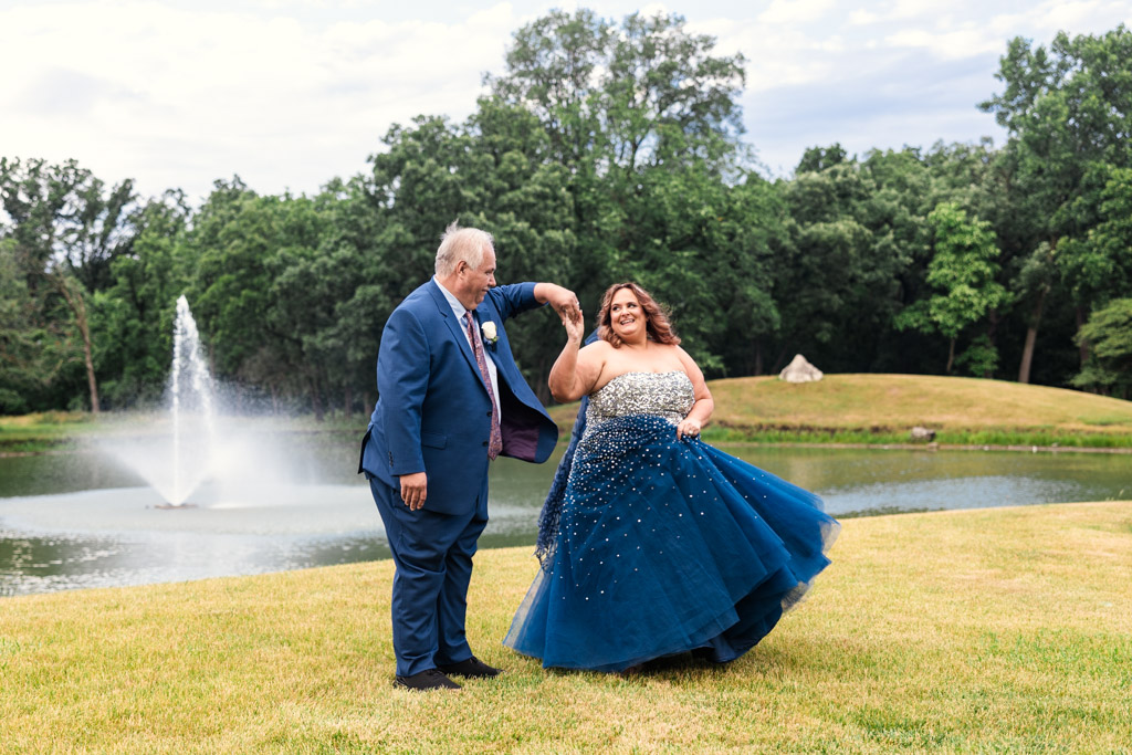 Bride and groom dance on the grass in front of fountain outside their summer wedding reception at Oak Brook Bath and Tennis