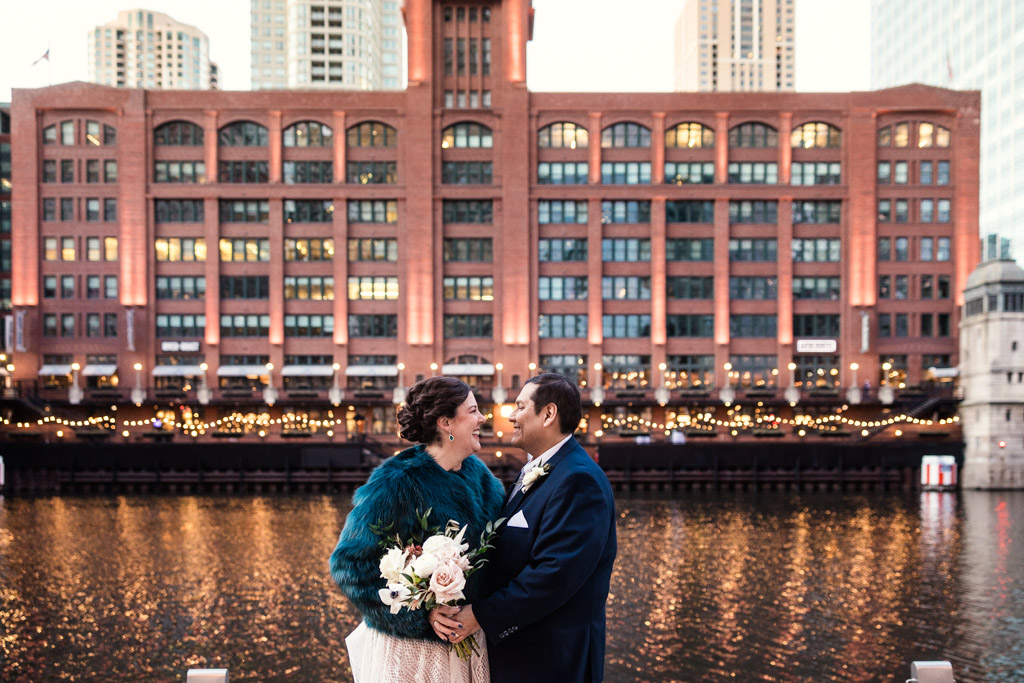 Bride and groom stand together at dusk on Chicago Riverwalk outside their River Roast Chicago wedding reception