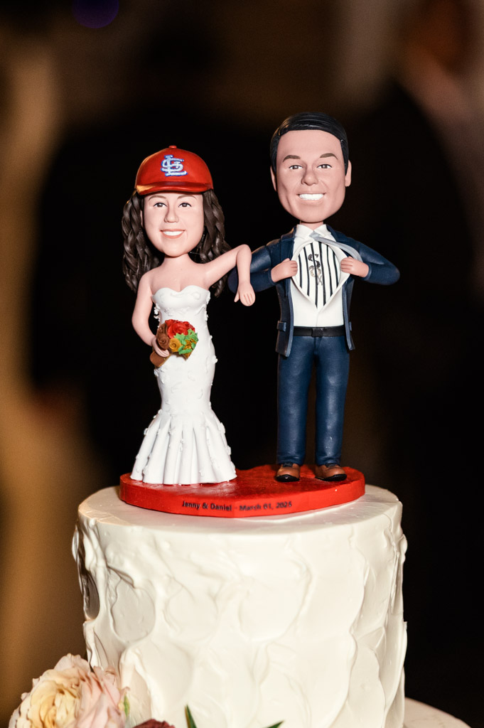 Custom wedding cake topper depicting bride in a gown and St. Louis Cardinals baseball cap and the groom opening his shirt and suit coat to display a Chicago White Sox jersey