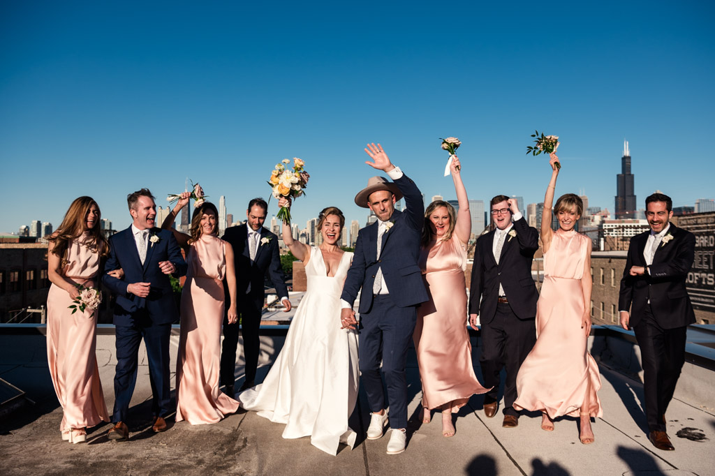 Bride, groom, and wedding party celebrating on a rooftop with a Chicago skyline in the background